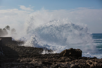 Tropical beach break, ocean wave crushing stone coastline, water splashes