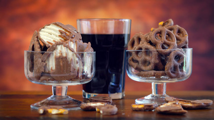 Sweet and salty chocolate covered salt and vingear potato chips and pretzels with cola drink, on rustic wood background.