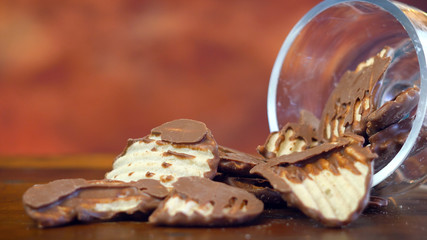 Sweet and salty snacks, chocolate covered salt and vinegar potato chips, macro close up on rustic wood background with copy space.