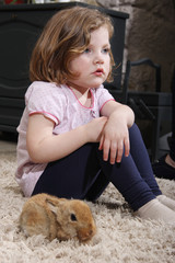 beautiful blonde little girl playing with a little bunny in the livingroom.