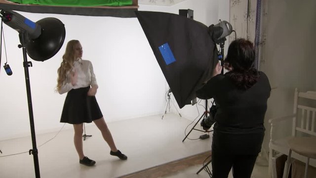 Studio photography. Female photographer working with young model. Teen girl in white shirt on set in photo studio. Backstage shot during indoor photoshoot.