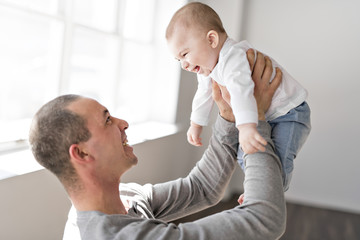 Father holds baby on a beautiful room with white windows