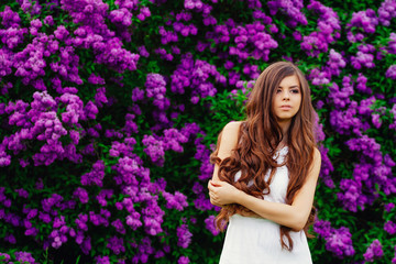 Naklejka premium Happy beautiful young woman with long hair in a blooming spring Park, the charming girl in a white dress with bright flowering trees, the girl on the background of flowering gardens