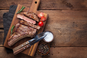 Fototapeta na wymiar Grilled cowboy beef steak, herbs and spices on a rustic wooden background. Top view with copy space for your text