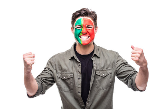 Handsome man supporter fan of Portugal national team painted flag face get happy victory screaming into a camera. Fans emotions.