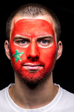 Portrait of handsome man face supporter fan of Morocco national team with painted flag face isolated on black background. Fans emotions.