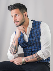 Trendy young man in studio shot wearing elegant vest and white shirt, looking away to a side