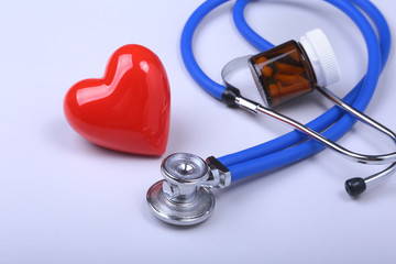 Stethoscope, red heart and assorted pills on white table with space for text.