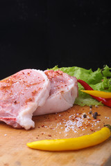 Raw steak, chop on a rustic cutting board with salt, pepper and grinder for spices . Black Background for copy space. Top View.