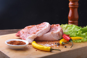 Raw steak, chop on a rustic cutting board with salt, pepper and grinder for spices . Black Background for copy space. Top View.