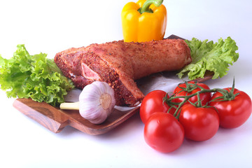 Raw pork knuckle and vegetables, garlic, tomatoes, bell pepper. spices and lettuce leaves on a cutting board. Selective focus. Ready for cooking.