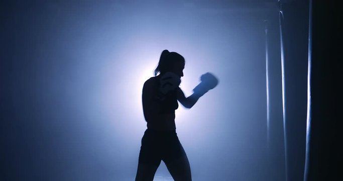 Beautiful female boxer training in a dark smoky room. Silhouette on a dark background
