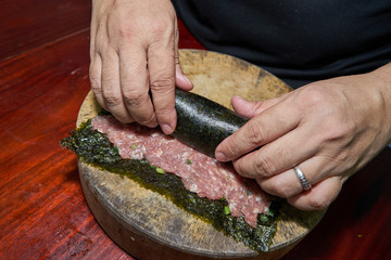 Woman hands to handle pork marinated tofu wrapped eggs on kelp on a wooden cutting board on a wooden table