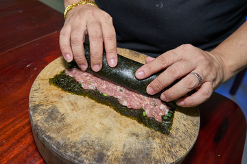 Woman hands to handle pork marinated tofu wrapped eggs on kelp on a wooden cutting board on a wooden table
