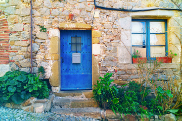 Fototapeta na wymiar Traditional wooden medieval vintage blue painted doors and window in Tossa de Mar, Spain, Catalonia, Costa Brava. Green plants near antique stone wall.
