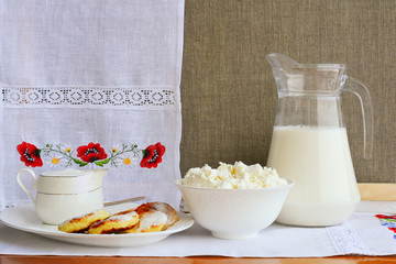 Still life of dairy products on a background of a towel with embroidery ..of red poppies. Cheesecake, home cottage cheese, milk in a jug, homemade sour cream.