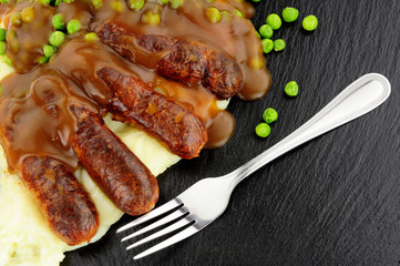 Sausages and mashed potato meal with garden peas on a slate background