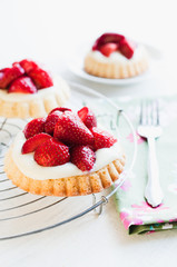 Strawberry tartlets with genoise sponge cake base and French vanilla custard pudding, called creme patissiere, for birthday or garden party on white wooden table