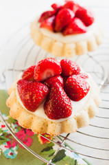 Strawberry tartlets with genoise sponge cake base and French vanilla custard pudding, called creme patissiere, for birthday or garden party on white wooden table