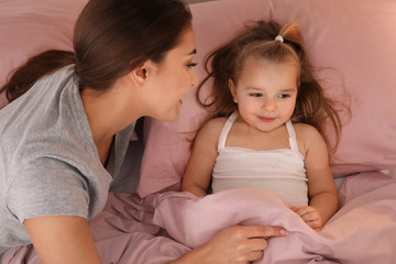 Mother putting her little daughter to bed at home