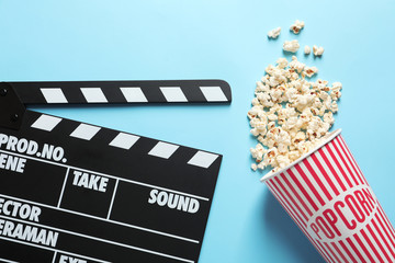 Clapperboard and popcorn on color background