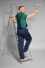 Young male decorator with paint roller on color background