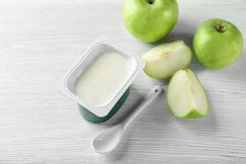 Plastic cup with yummy apple yogurt on wooden table