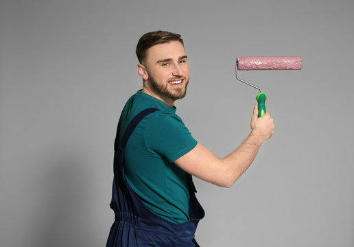 Young male decorator with paint roller on color background