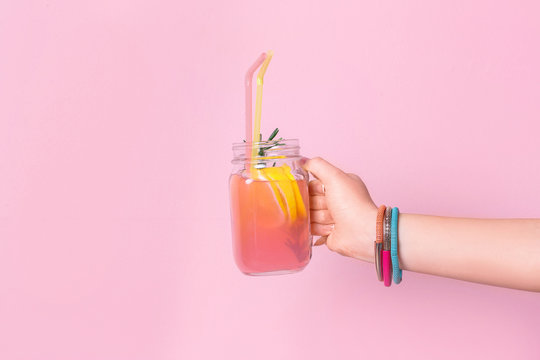 Young woman holding mason jar with lemonade on color background