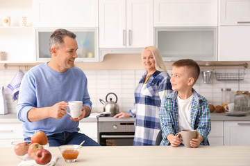 Happy senior couple having breakfast with little grandson in kitchen