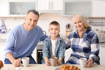 Happy senior couple having breakfast with little grandson in kitchen
