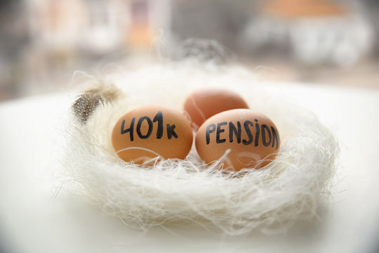 Eggs with words "Pension" and "401k" in nest on blurred background