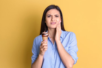 Young woman with sensitive teeth and cold ice cream on color background