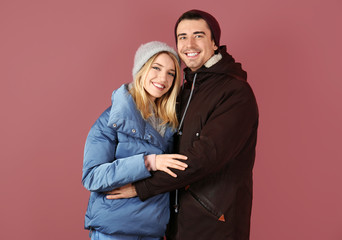 Young couple in warm clothing on color background. Ready for winter vacation