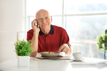 Elderly man talking on phone while having breakfast at home