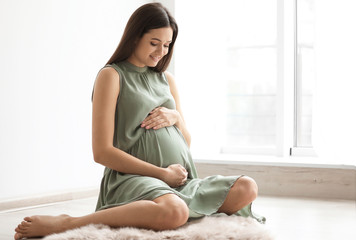 Young pregnant woman sitting on floor near window at home