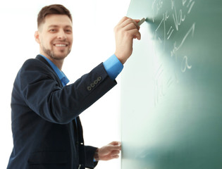 Male teacher writing on blackboard in classroom