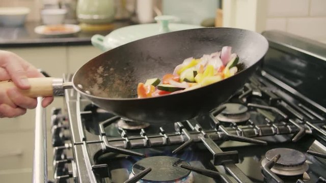 Man Tossing Healthy Vegetables In Wok On Stove At Kitchen