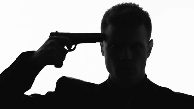 Silhouette of serious male holding pistol and preparing to kill himself, suicide