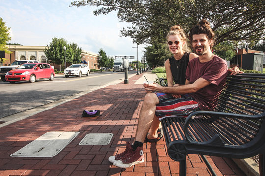 happy young hipp couple sitting on a bench on the sidewalk