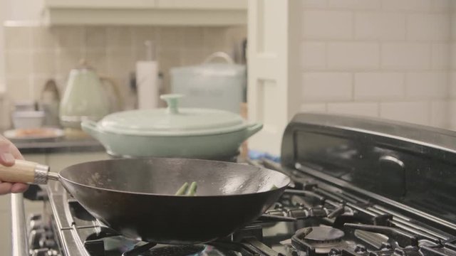 Man Tossing Green Beans In Wok On Stove At Kitchen