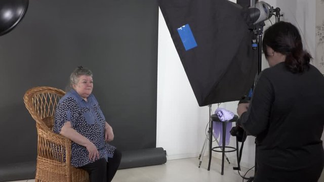 Studio portrait photography. Senior woman poses for photographer. Female photographer working in photo studio photographing elderly woman. Backstage shot during photoshoot.