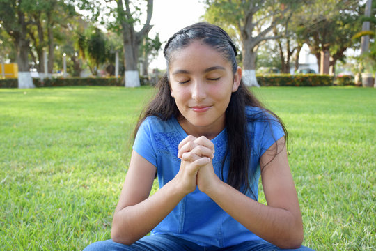 pretty girl seated on grass praying 