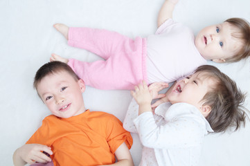 Fototapeta na wymiar happy laughing kids, three children different ages lying, portrait of boy, little girl and baby girl, happiness in childhood of siblings, living in big family with three children