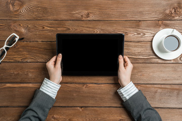 Top view of businesswoman sitting at wooden table and working with tablet