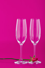 Two wine glasses with rose flower on pink background