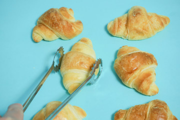 Bread, croissant. Image to have bread with a tong, display bread at store.  パン、クロワッサン　トングでパンを取る、店頭でパンを並べるなどのイメージ　水色背景