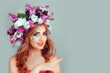 Happy beautiful young woman with floral lilac headband shows a finger pointing