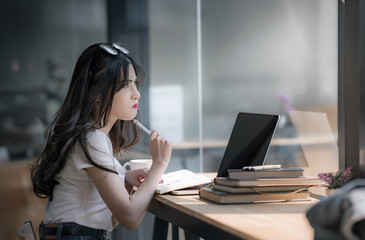 Confused young woman holding pen touches the shin having problem with her job while using laptop