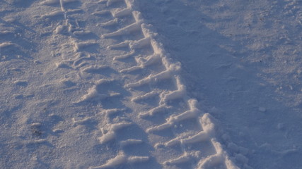 Traces of heavy machinery on a snowy road in the rays of the rising sun.
